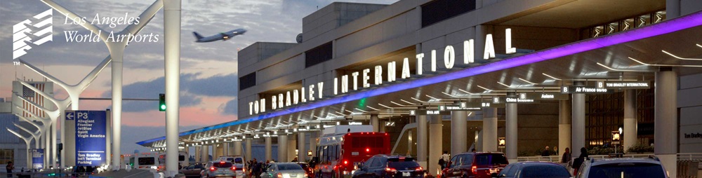 Night shot of Tom Bradley International Terminal. The sun has almost setting, automatically turning on the lights at LAX, including the breaklights of over a dozen vehicles. In the distance, an airplane takes off towards the pacific ocean.